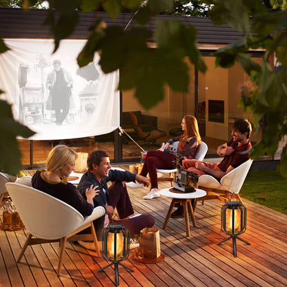People watching a movie on a screen outdoors with lanterns on a wooden deck.